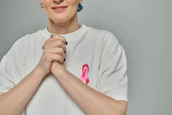 A woman wears a white t-shirt with a pink ribbon, a symbol of breast cancer awareness, clasped hands in front of her chest. — Stock Photo