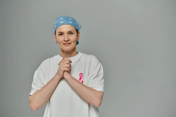 Una donna con i capelli corti e un nastro rosa sulla camicia poggia su uno sfondo grigio. — Foto stock