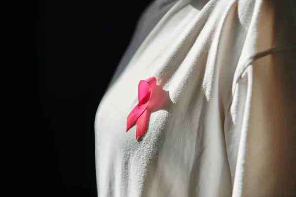 A close-up of a pink ribbon pinned to a woman's shirt, symbolizing breast cancer awareness. — Stock Photo