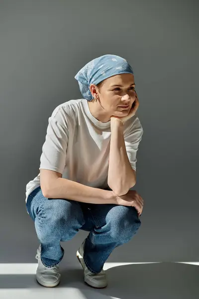 Une femme portant des vêtements décontractés, assise avec son menton reposant sur sa main sur un fond gris. — Photo de stock