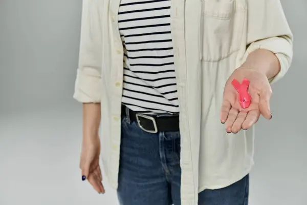 Cropped woman holds out her hand, displaying a pink ribbon in support of breast cancer awareness. — Stock Photo