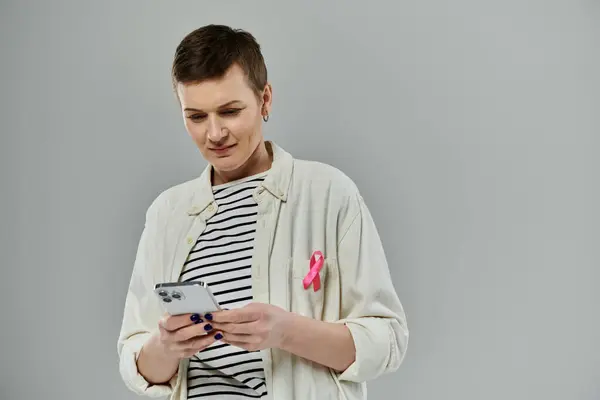 A woman with short hair, wearing a white shirt and a pink ribbon, uses her phone. — Stock Photo