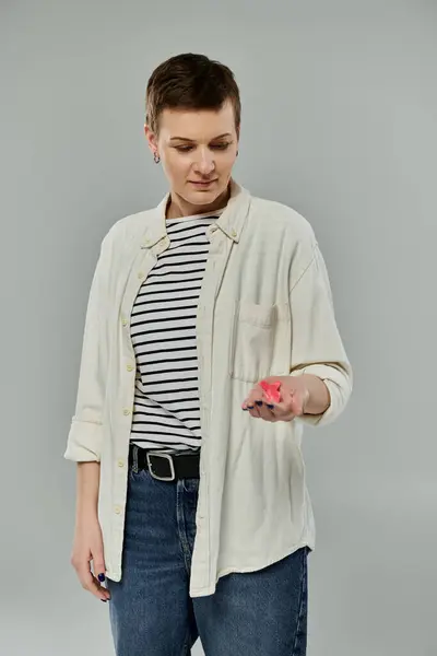 A woman with short hair, wearing a white shirt and jeans, holds a pink ribbon in her hand against a grey backdrop. — Stock Photo