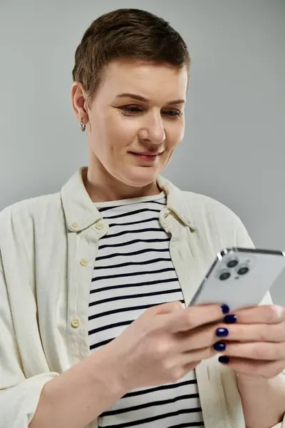 A woman with short hair and a casual outfit smiles as she uses a smartphone. — Stock Photo