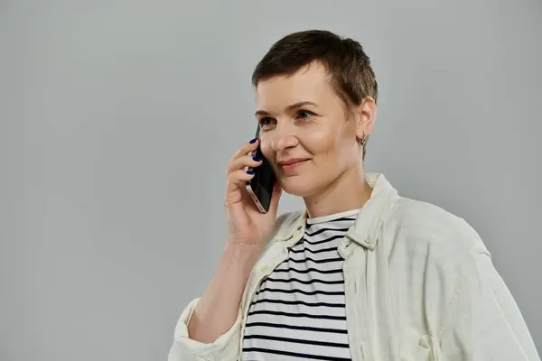 A woman with short brown hair wearing a white shirt over a striped shirt is on a phone call. — Stock Photo