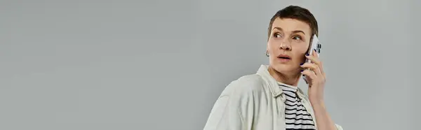 A woman with short hair in casual attire is surprised by a phone call. Her expression is shocked and she is looking over her shoulder. — Stock Photo