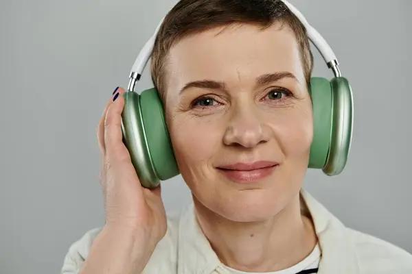 A woman with short hair smiles as she listens to music through headphones. — Stock Photo