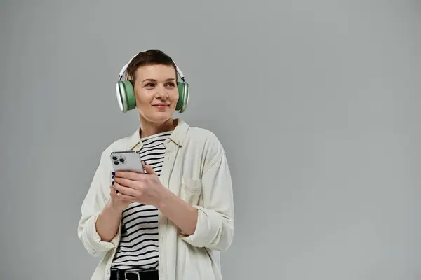 A woman with short hair, wearing casual attire, uses her smartphone while wearing headphones. — Stock Photo