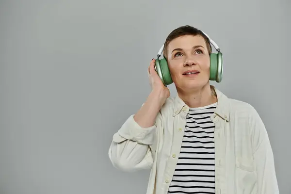 A woman with short hair and casual attire listens to music with headphones on, gazing upwards. — Stock Photo