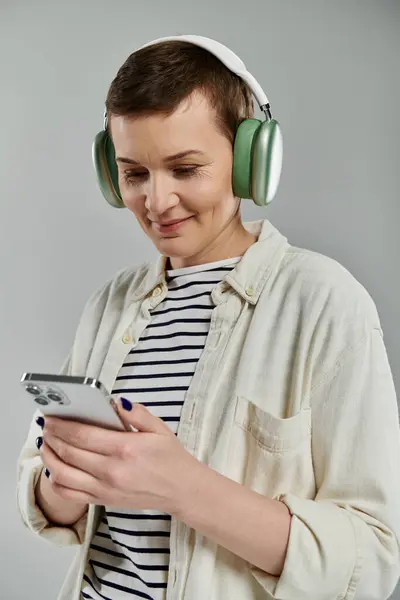 A woman with short hair, wearing a white shirt and headphones, looks down at her phone. — Stock Photo
