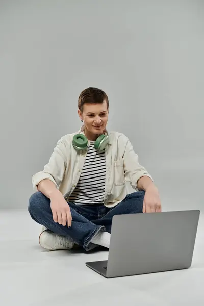 A woman with short hair sits on the floor wearing casual attire and using a laptop. — Stock Photo