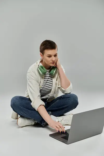 Eine Frau mit kurzen Haaren sitzt im Schneidersitz auf dem Boden und arbeitet an einem Laptop. — Stockfoto