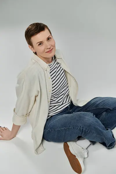 A woman with short hair, wearing casual clothes, sits on a white floor, smiling as she uses a device. — Stock Photo