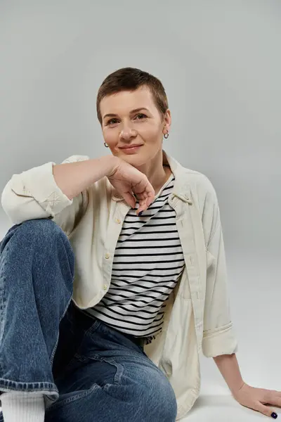 A woman with short hair and a confident smile sits casually against a light background. — Stock Photo
