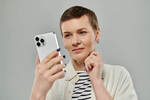 A woman with short hair, wearing casual attire, holds a smartphone and stares intently at the screen, her expression thoughtful. — Stock Photo