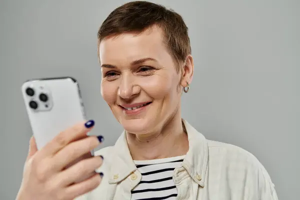 A woman with short hair smiles as she uses her phone, holding it with both hands. — Stock Photo