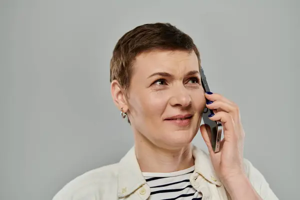 A woman with short hair, wearing a casual outfit, talks on the phone with a slight smile. — Stock Photo