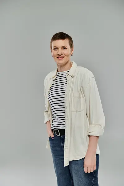 A woman with short hair, dressed in casual clothing, smiles confidently against a gray background. — Stock Photo