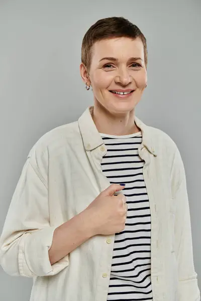 A woman with short hair smiles while standing in front of a gray background. — Stock Photo