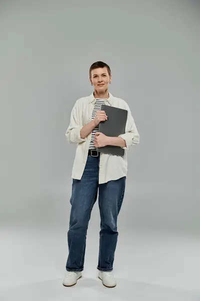 A woman with short hair, wearing a white shirt and jeans, stands confidently while holding a device. — Stock Photo