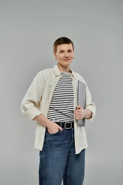 Confident woman with short hair holds laptop, wearing white shirt, striped top, and jeans — Stock Photo