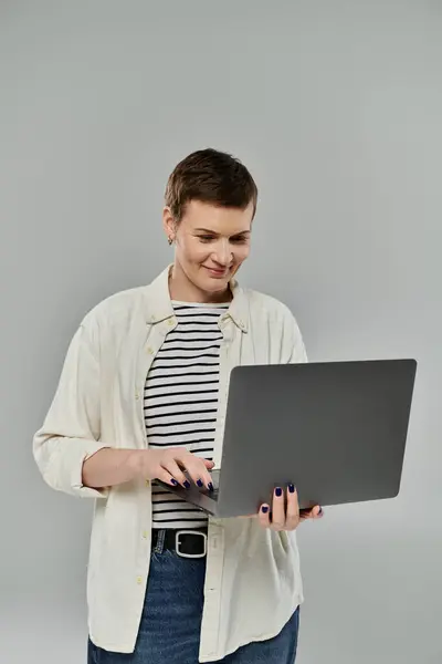 A woman with short hair uses a laptop, smiling as she looks at the screen. — Stock Photo