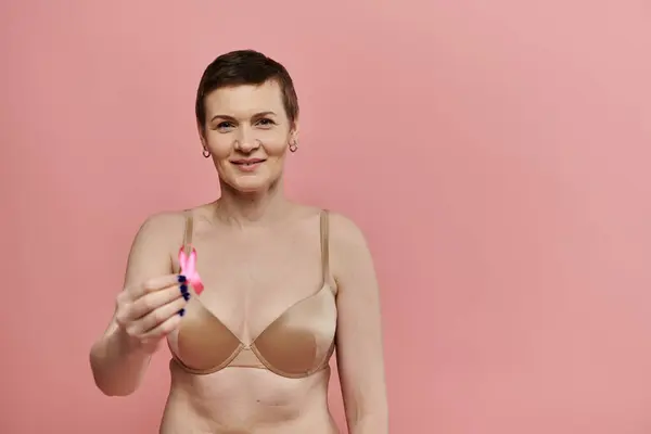 A woman with short hair smiles confidently while holding a pink ribbon in front of her chest. — Stock Photo