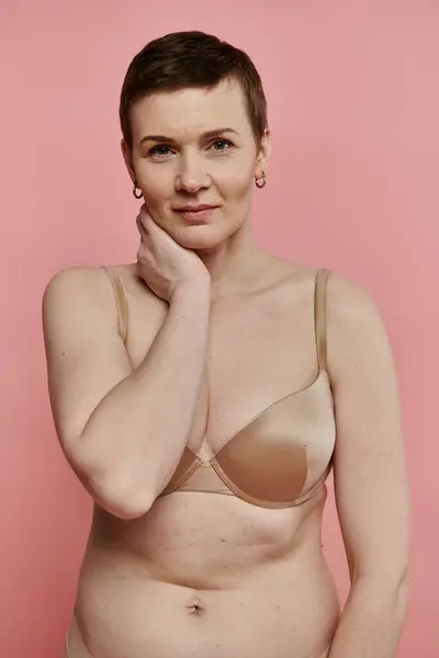 A woman with short hair, wearing a bra, stands in front of a pink background. — Stock Photo