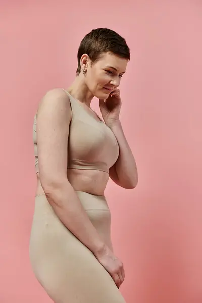 Une femme aux cheveux courts, portant un soutien-gorge, se tient sur un fond rose. — Stock Photo