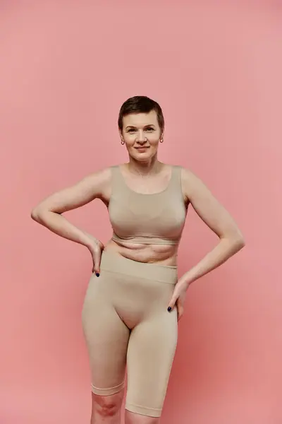 A woman with short hair poses confidently standing against a pink background. — Stock Photo