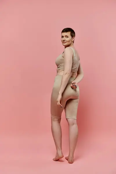 A woman with short hair, wearing a bra, stands confidently against a pink background. — Stock Photo