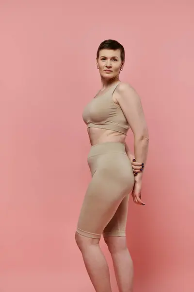 Una donna con i capelli corti si trova in un reggiseno beige e pantaloncini, guardando verso la fotocamera. — Foto stock