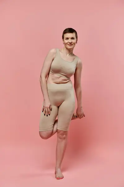 A woman with short hair, wearing a bra and shorts, poses confidently against a pink background. — Stock Photo