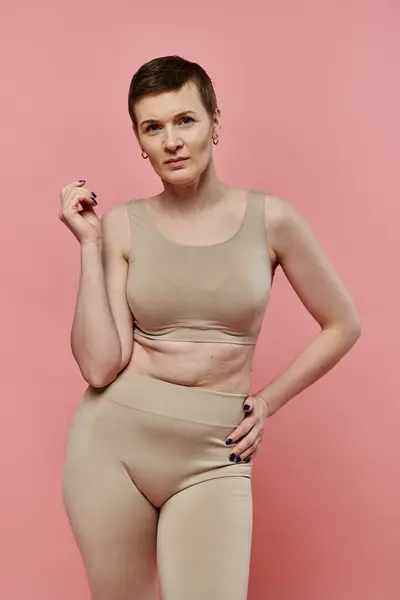 Una donna con i capelli corti sta in un reggiseno beige, consapevolezza del cancro al seno. — Foto stock