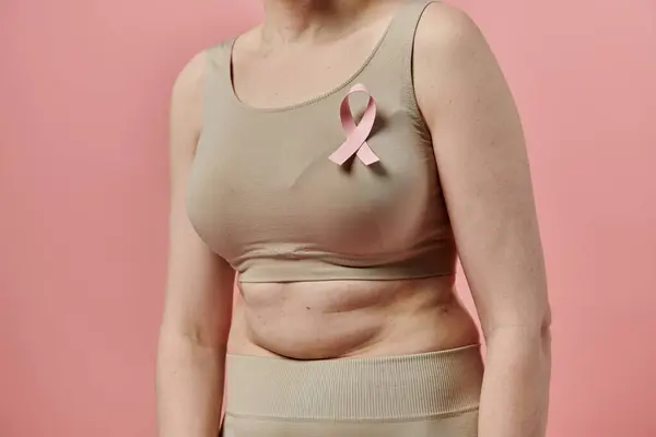 A woman with short hair stands with a pink ribbon on her bra, demonstrating support for breast cancer awareness. — Stock Photo