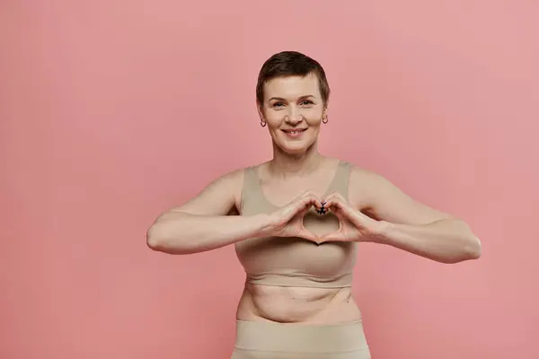 Kurzhaarige Frau formt Herz mit Händen vor rosa Hintergrund und symbolisiert Brustkrebs-Sensibilisierung — Stockfoto