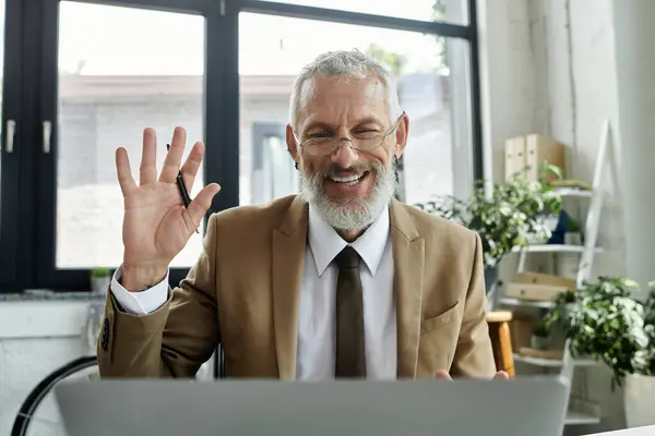 Uomo di mezza età in giacca e cravatta sorride mentre insegna online in un ufficio moderno con un computer portatile di fronte a lui — Foto stock
