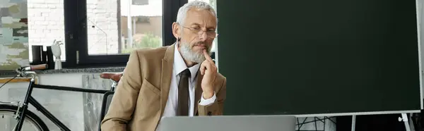 A mature man with a beard sits in front of a laptop, thoughtfully teaching online, lgbtq teacher — Stock Photo
