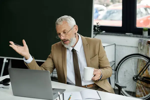 Um homem barbudo, de meia-idade, vestido com um terno e gravata, senta-se em uma mesa na frente de um laptop, gesticulando enquanto dá aulas on-line, lgbtq professor — Fotografia de Stock