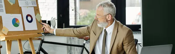 Un professeur LGBTQ mature avec une barbe pointe vers un tableau sur un tableau blanc tout en enseignant en ligne. — Photo de stock