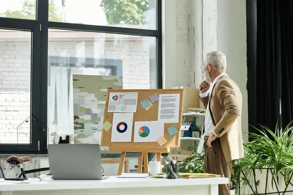 Middle-aged man in brown suit in home office, by window, looking at whiteboard with charts and notes, ready to teach online — Stock Photo