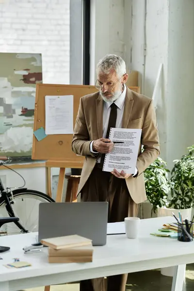 Ein Lehrer mittleren Alters mit Bart unterrichtet seine Online-Klasse von zu Hause aus, hält eine Zeitung in der Hand und bedient sich eines Laptops.. — Stockfoto