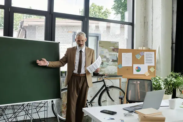 A bearded teacher gestures at a whiteboard in a modern classroom conducting an online lesson — Stock Photo