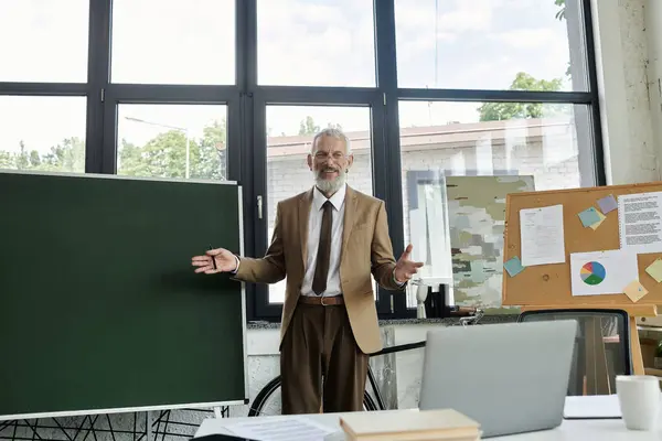Зрілий бородатий вчитель навчає своїх студентів через ноутбук у яскравому класі. — стокове фото