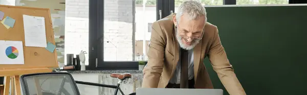 Ein reifer, bärtiger Lehrer lächelt, während er einen Laptop benutzt, um online zu unterrichten. — Stockfoto