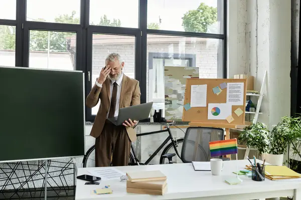A mature LGBTQ teacher, with a beard, teaches a class online using a laptop in his modern classroom. — Stock Photo