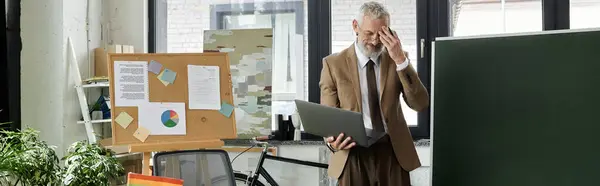 A mature LGBTQ teacher with a beard, wearing a suit, looks weary while teaching online using a laptop. — Stock Photo