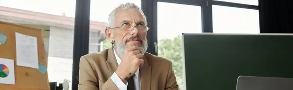 A mature LGBTQ teacher with a beard contemplates his next lesson while teaching online from his laptop. — Stock Photo