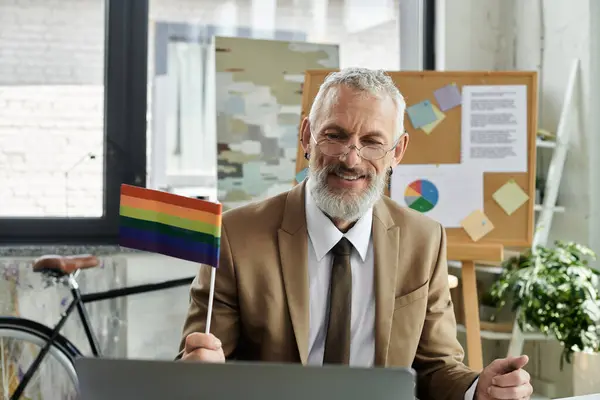 A mature teacher with a beard smiles and holds a rainbow pride flag while teaching online. — Stock Photo