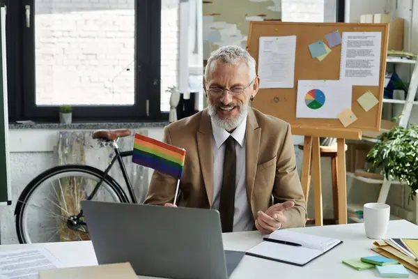 A mature LGBTQ teacher with a beard teaches an online class, smiling at the camera while holding a rainbow flag. — Stock Photo
